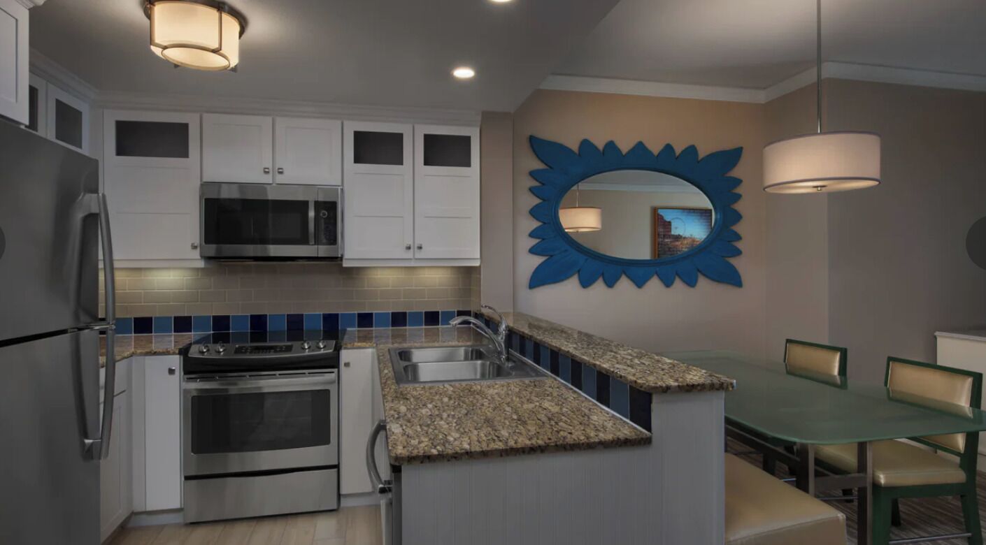 A modern kitchen with stainless steel appliances, a granite countertop, and a dining area with a green table and chairs.