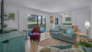 A spacious living room with a grey sofa, red armchair, and a blue cabinet. - Seascape Resort Villa -33B*Quiet Villa*Pools*Beachy (Miramar Beach)