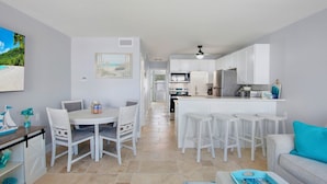 Una cocina moderna con armarios blancos, una isla central con taburetes y una zona de comedor con mesa y sillas.
