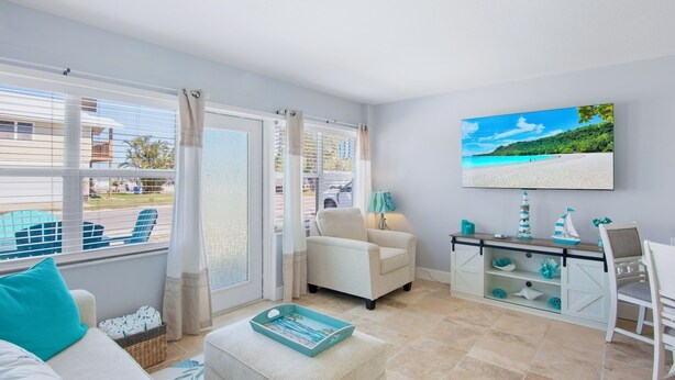 Una sala de estar con vista a la playa, un sofá, una silla, una mesa de centro y un televisor en la pared.