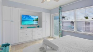 Un dormitorio con cama, televisor en la pared y ventana con persianas.