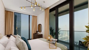 Un dormitorio moderno con una cama grande, una mesita de noche con espejo y vistas a un paisaje urbano a través de ventanales de piso a techo.