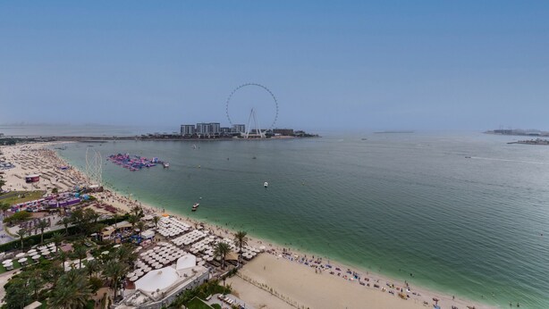 Una playa con noria, agua cristalina y sombrillas.