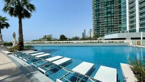 Una piscina con sillones de descanso, palmeras y un edificio moderno al fondo.