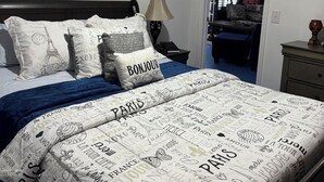 Ein Schlafzimmer mit einem Bett, einem Nachttisch, einer Lampe und einer Tür zu einem anderen Raum.