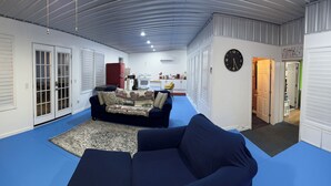 Ein kompakter Wohnraum mit blauem Boden, einer Couch, einem gemusterten Teppich und einer Küchenzeile im Hintergrund.