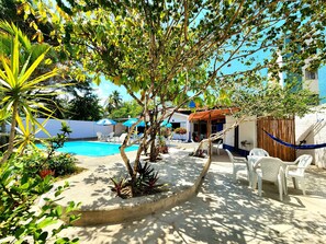 A pool area with lounge chairs and umbrellas, surrounded by greenery and a wooden fence. - Pousada Suítes do Atlântico (Ilhéus)