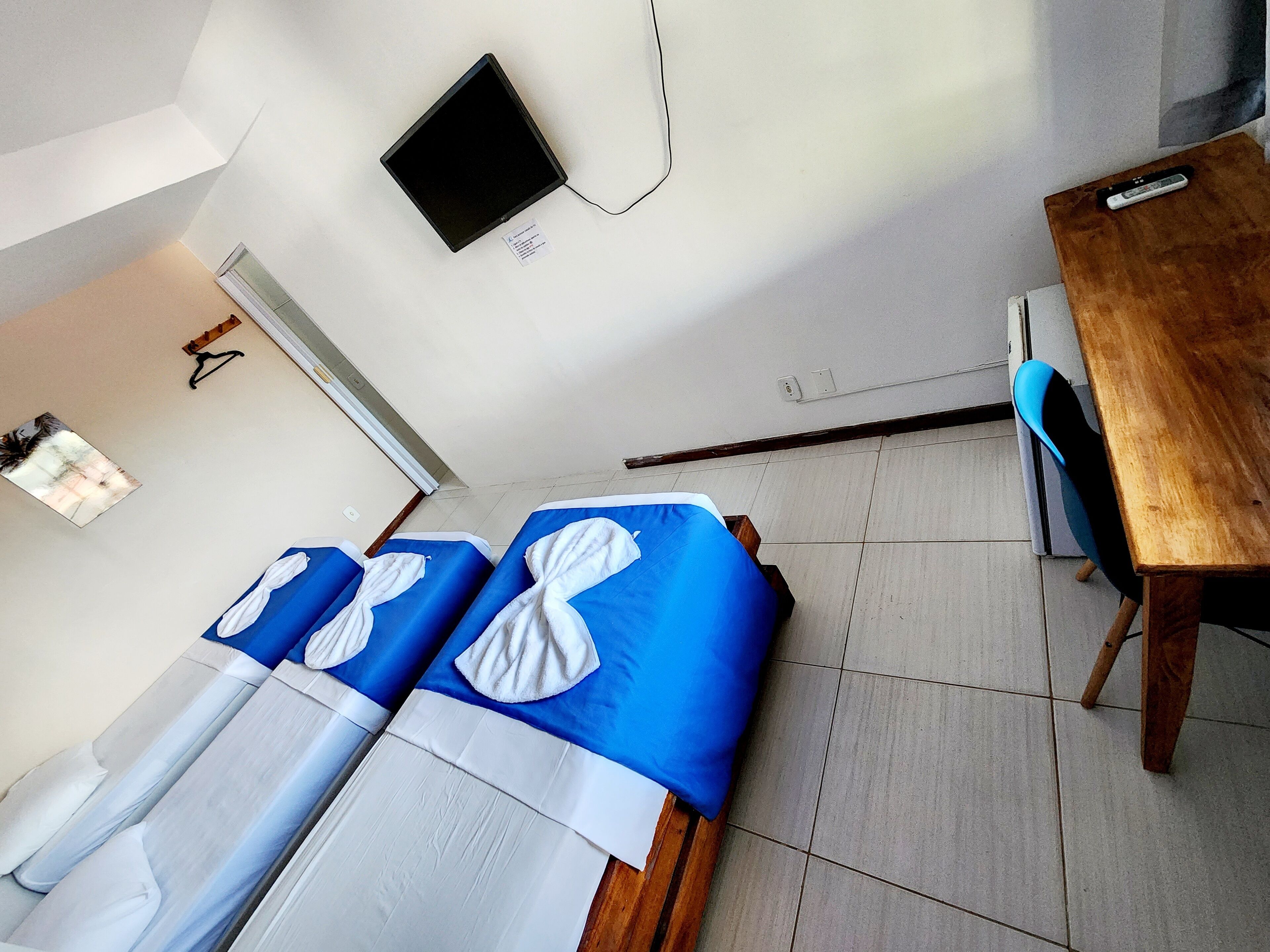 Een kamer met twee bedden, een houten tafel, een stoel, een televisie en een raam.