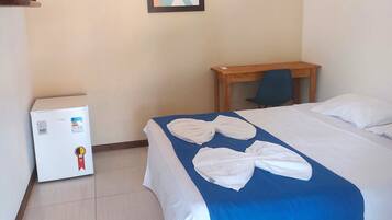 A hotel room with a bed, a small table, a refrigerator, and a framed picture on the wall.