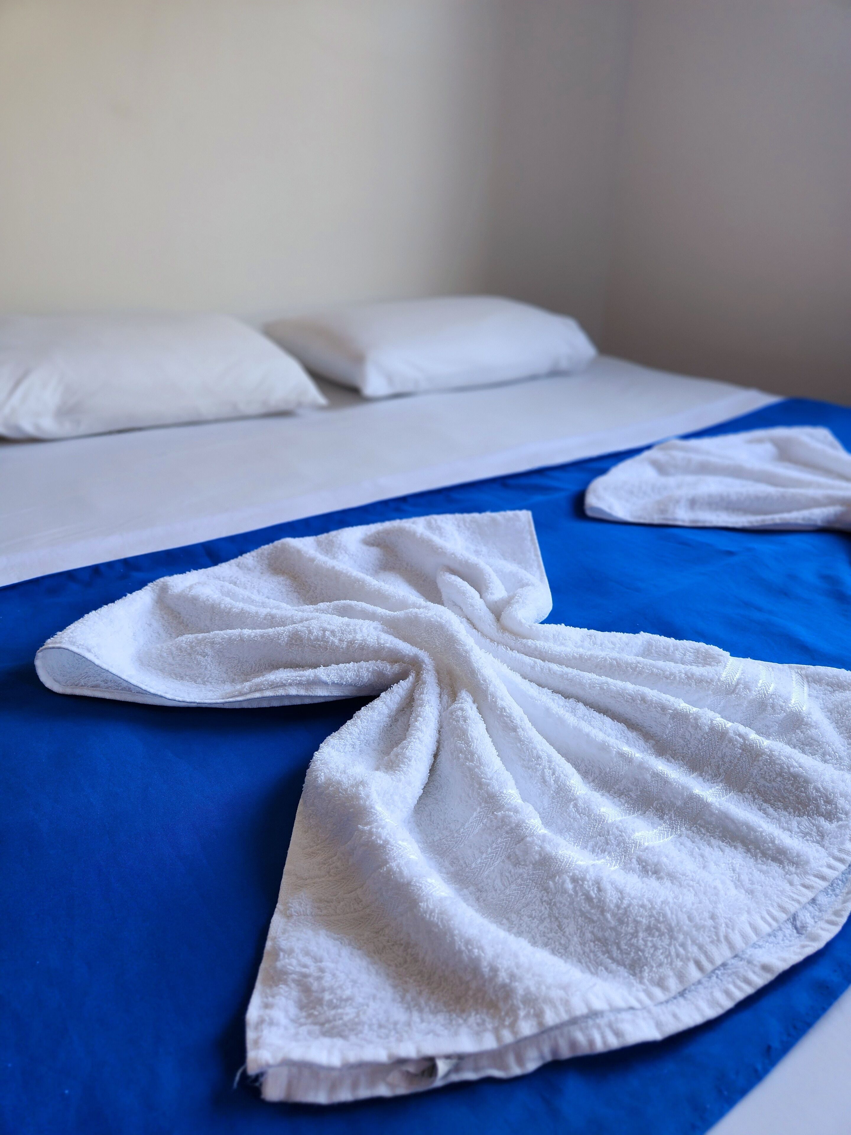 A bed with a blue bedspread and a white towel folded on it.