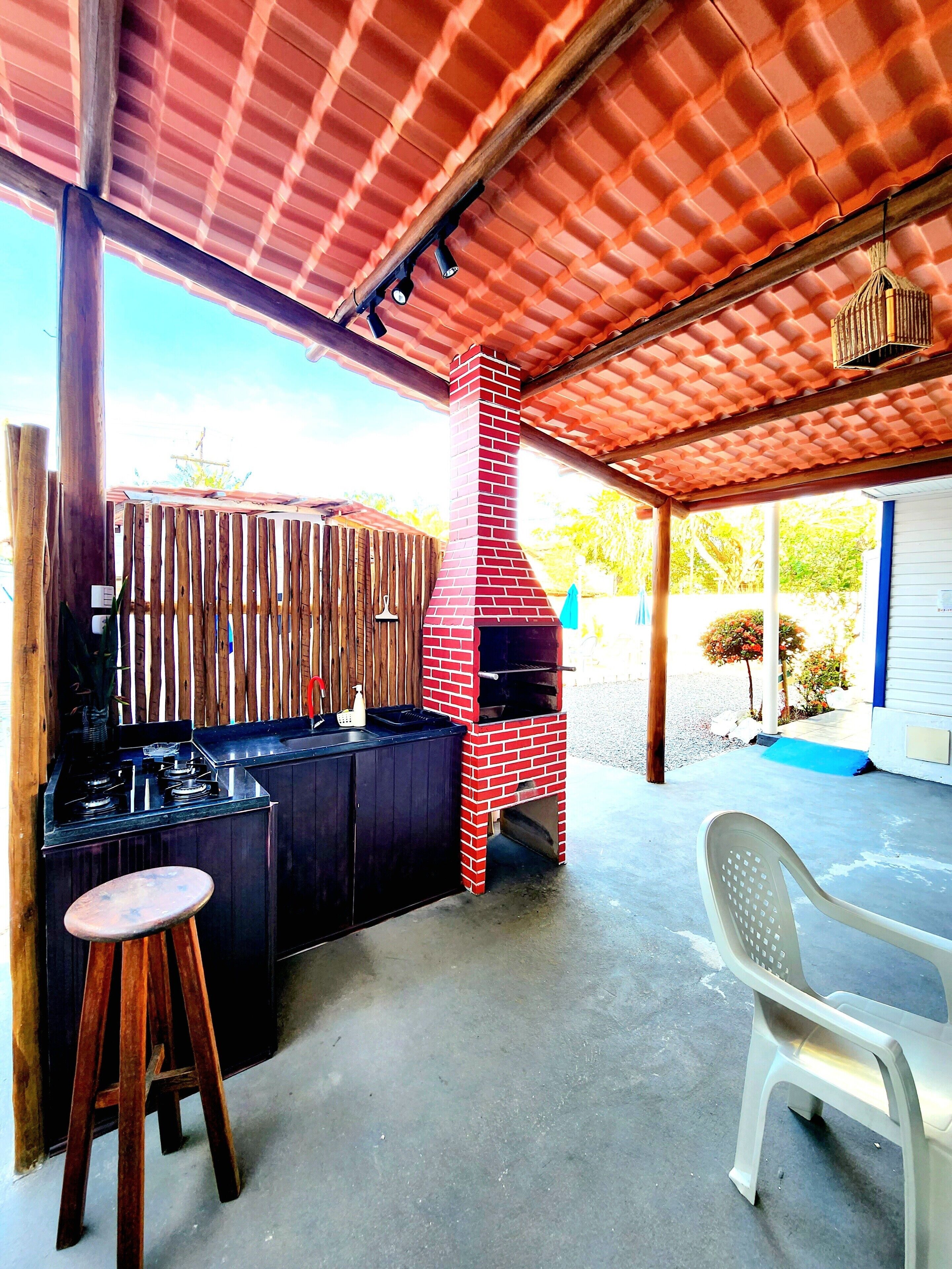 Un área de cocina al aire libre con horno de ladrillo, taburetes de madera y un porche cubierto.