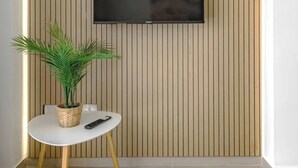 A modern room with a TV mounted on a wooden slat wall, a small round table with a plant and remote, and a tiled floor. - Stunning apartment in Costa Adeje with heated pool. (Costa Adeje)