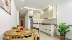 A modern kitchen with a microwave, refrigerator, and a wooden dining table with chairs. - Stunning apartment in Costa Adeje with heated pool. (Costa Adeje)