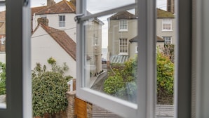 Une vue à travers une fenêtre donnant sur une rue résidentielle, avec des maisons, une rue étroite et quelques espaces verts.
