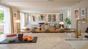 Un espace repas moderne avec un comptoir en marbre, une table à manger en bois pour quatre personnes et une vue sur le salon en arrière-plan.