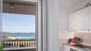 A modern kitchen with white cabinets, a built-in oven, and a view of the sea through an open door. - Harenae Beach Gataway by Wonderful Italy (Olbia)