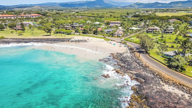 Ein Küstenresort mit Strand, klarem türkisblauem Wasser und einem Bergpanorama im Hintergrund.