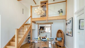 Ein großzügiges Loft mit einer Holztreppe, einem Essbereich mit rundem Tisch und einer im Hintergrund sichtbaren Küche.