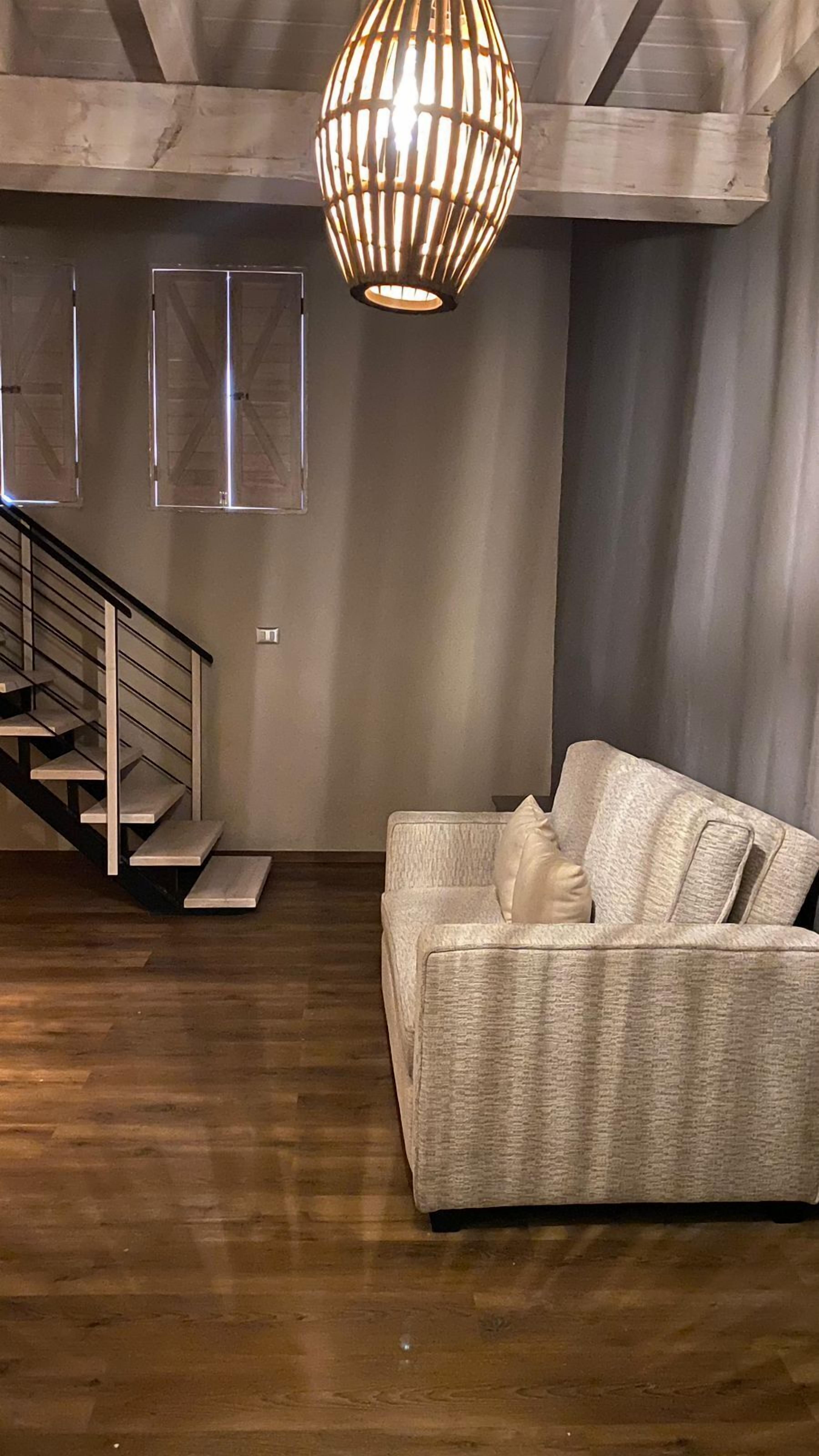 Una sala de estar moderna con una escalera de madera, una lámpara colgante y un sofá con textura.