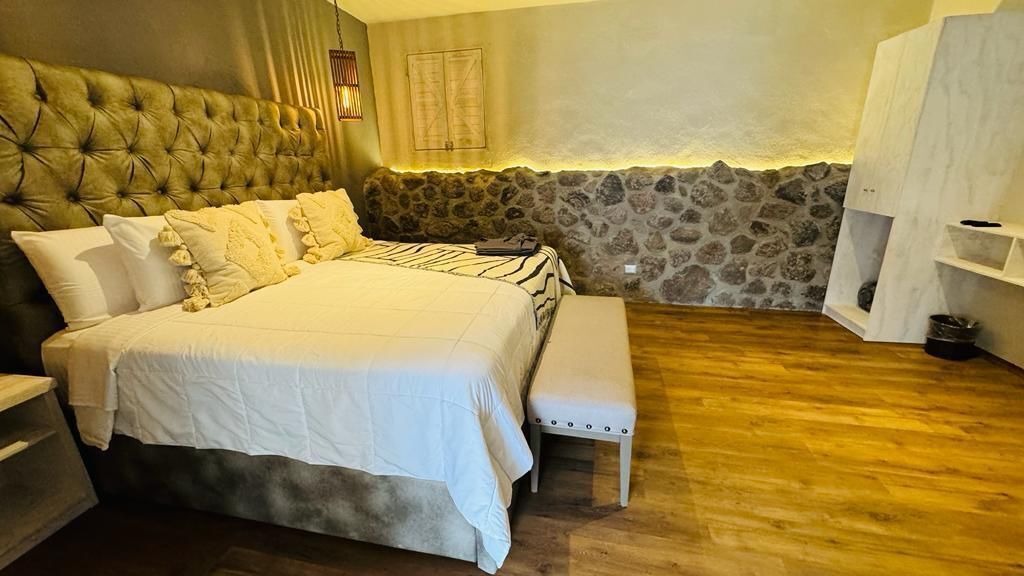 Un dormitorio con una cama grande, un banco, una pared de piedra y suelo de madera.