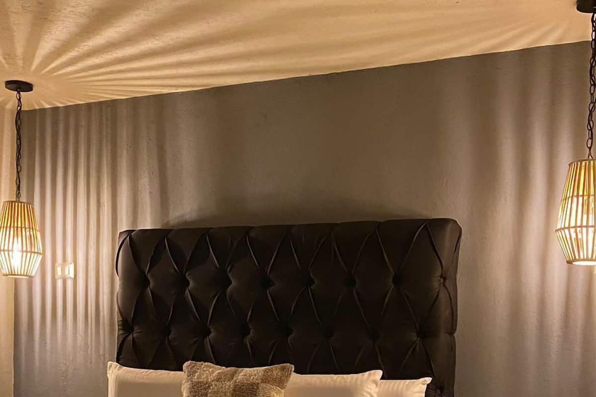 A neatly made bed with a tufted headboard, white linens, and a folded blanket on the footboard. There is a bedside table with a lamp on it.