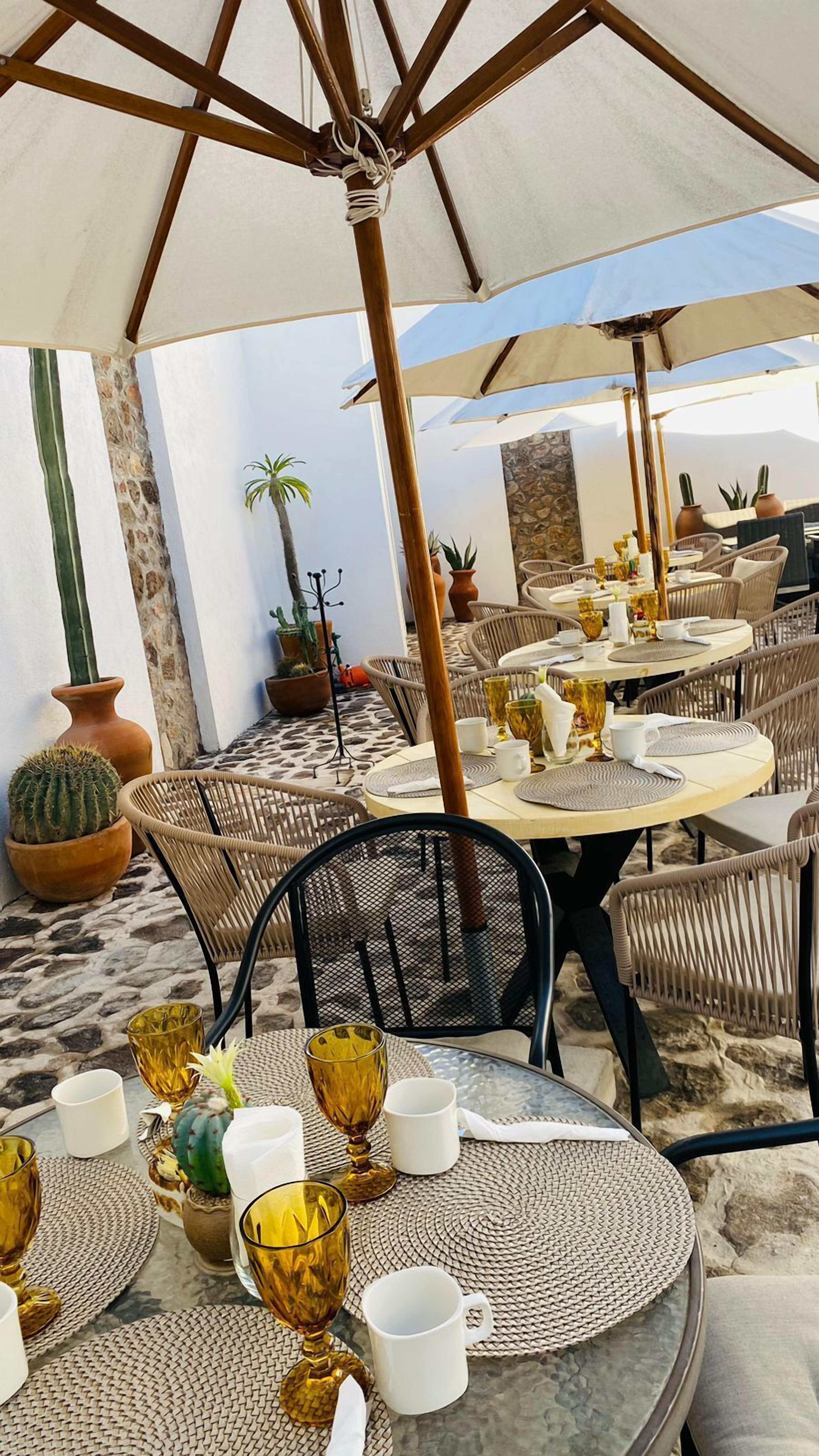 An outdoor dining area with round tables, wicker chairs, and umbrellas providing shade.