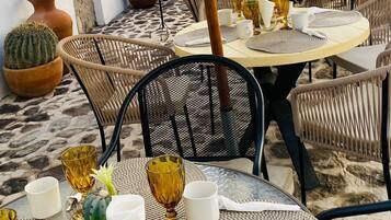 An outdoor dining area with round tables, wicker chairs, and umbrellas providing shade.
