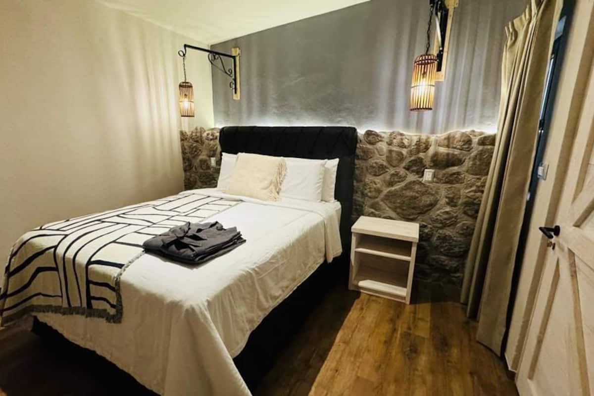 A bedroom with a bed, a nightstand, a stone accent wall, and hanging lights.