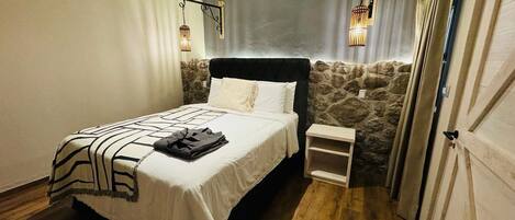 Une chambre avec un lit, une table de chevet, un mur décoratif en pierre et des luminaires suspendus.