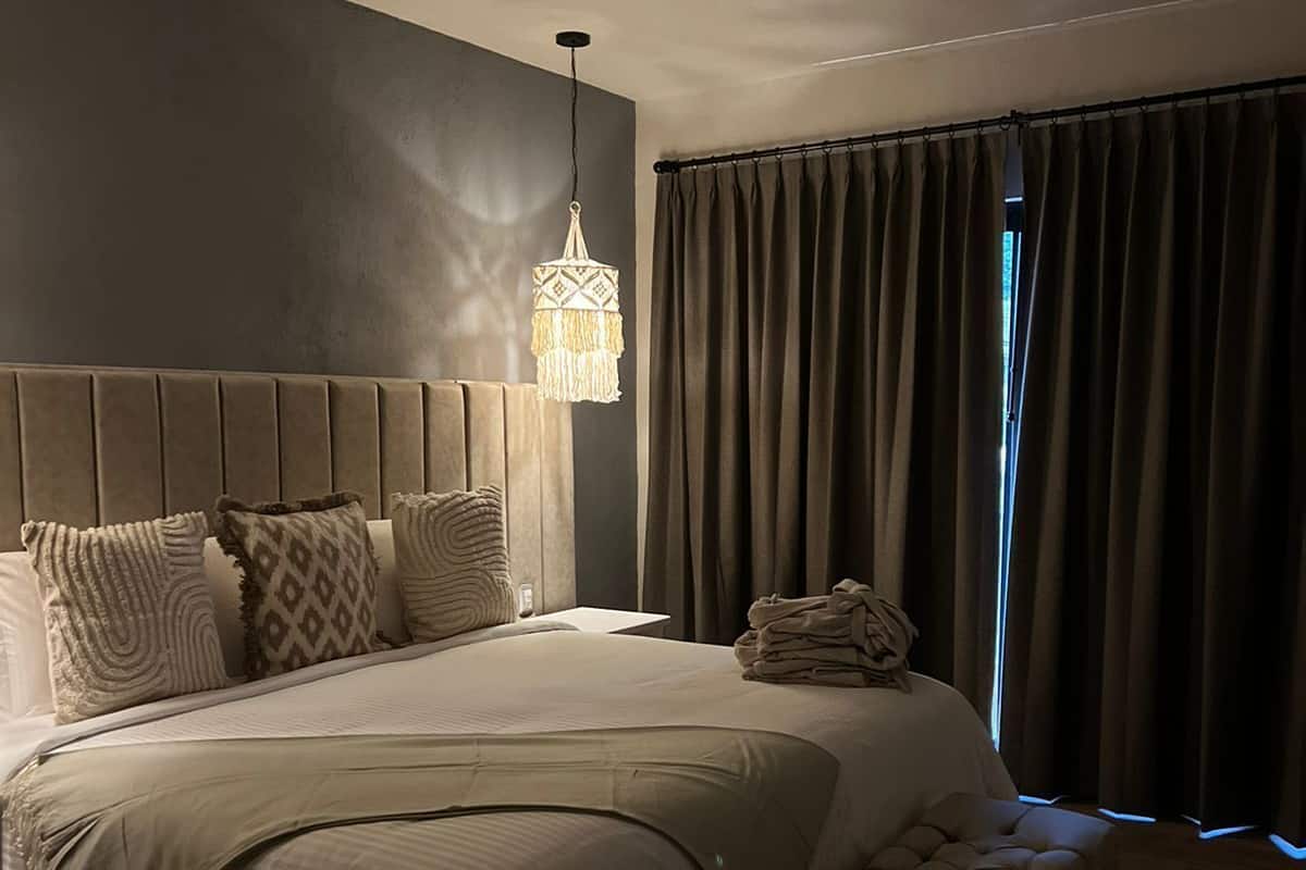 A neatly made bed with a headboard, a hanging light fixture, and a window with curtains.