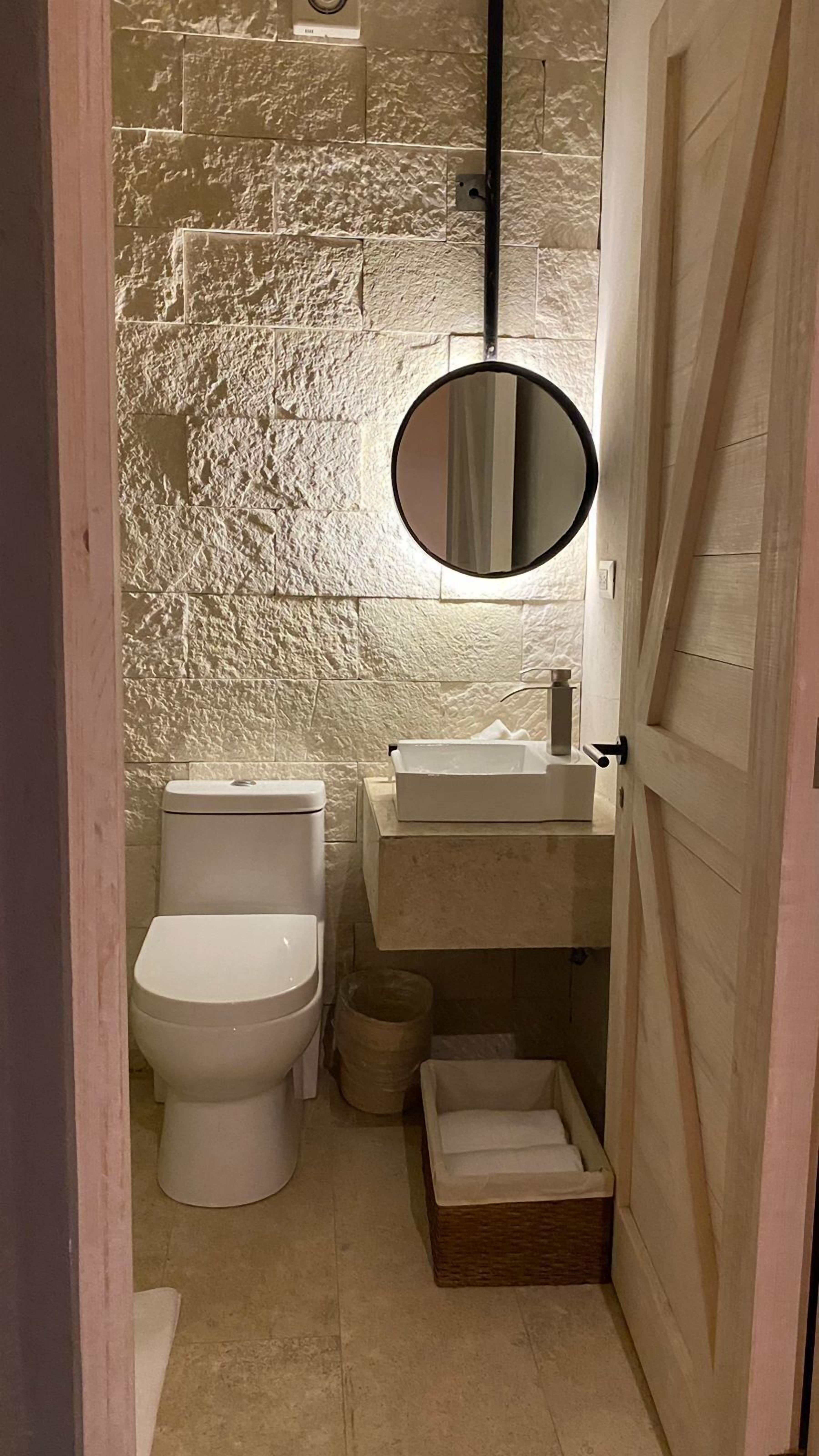 A compact bathroom with a white toilet, a sink with a mirror above it, and a small wicker basket on the floor.