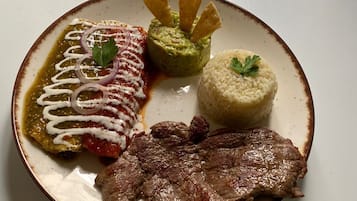 Un plato con bistec, arroz, guacamole y salsa roja con aros de cebolla.