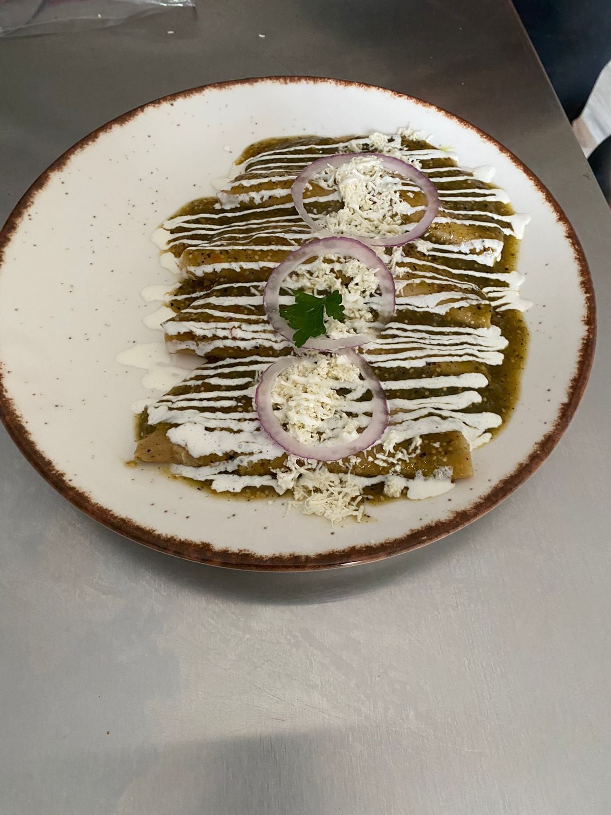 A plate of enchiladas topped with sour cream, cheese, and a green sauce, garnished with red onion rings and a leaf.