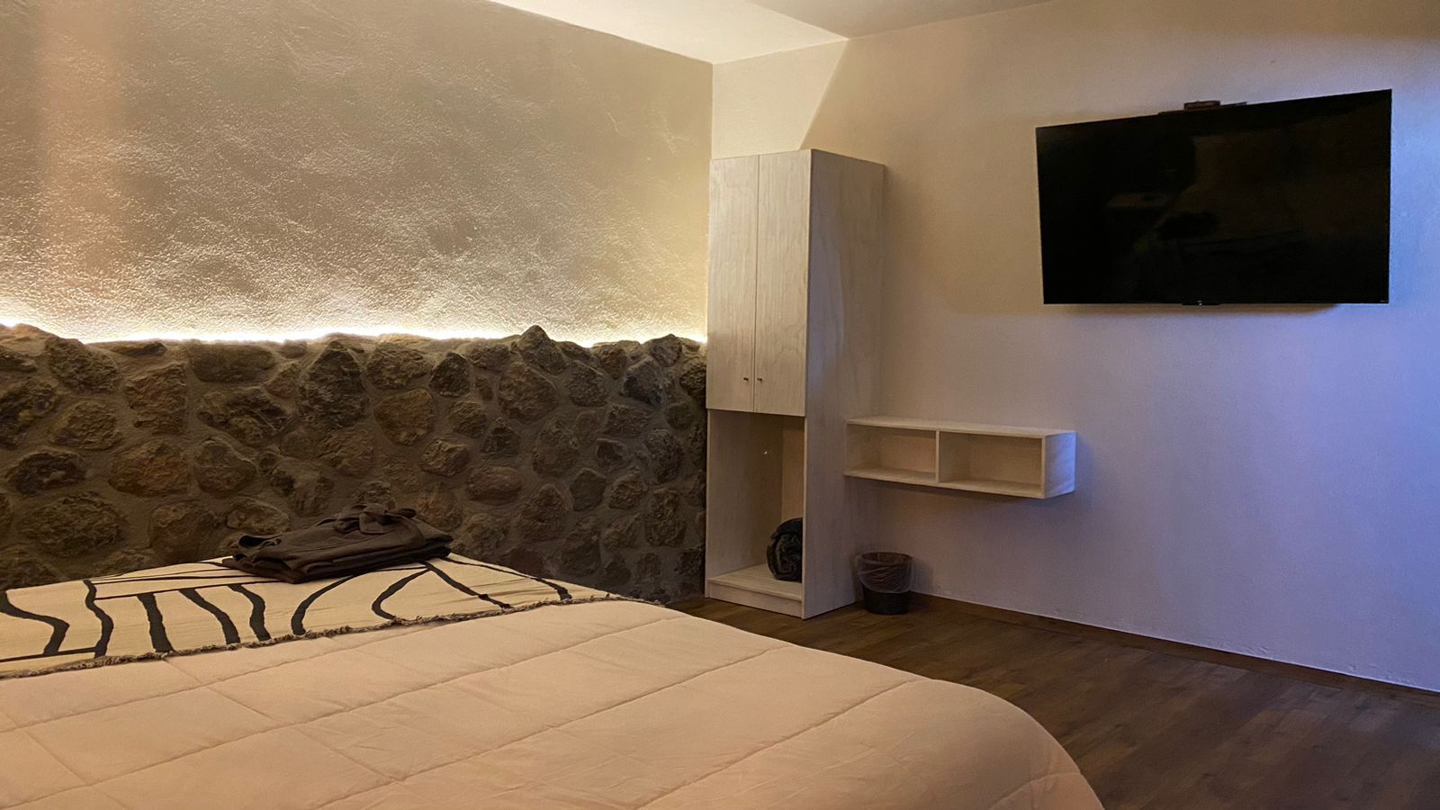 A bedroom with a stone wall, a bed, a wardrobe, a TV, and a small shelf.