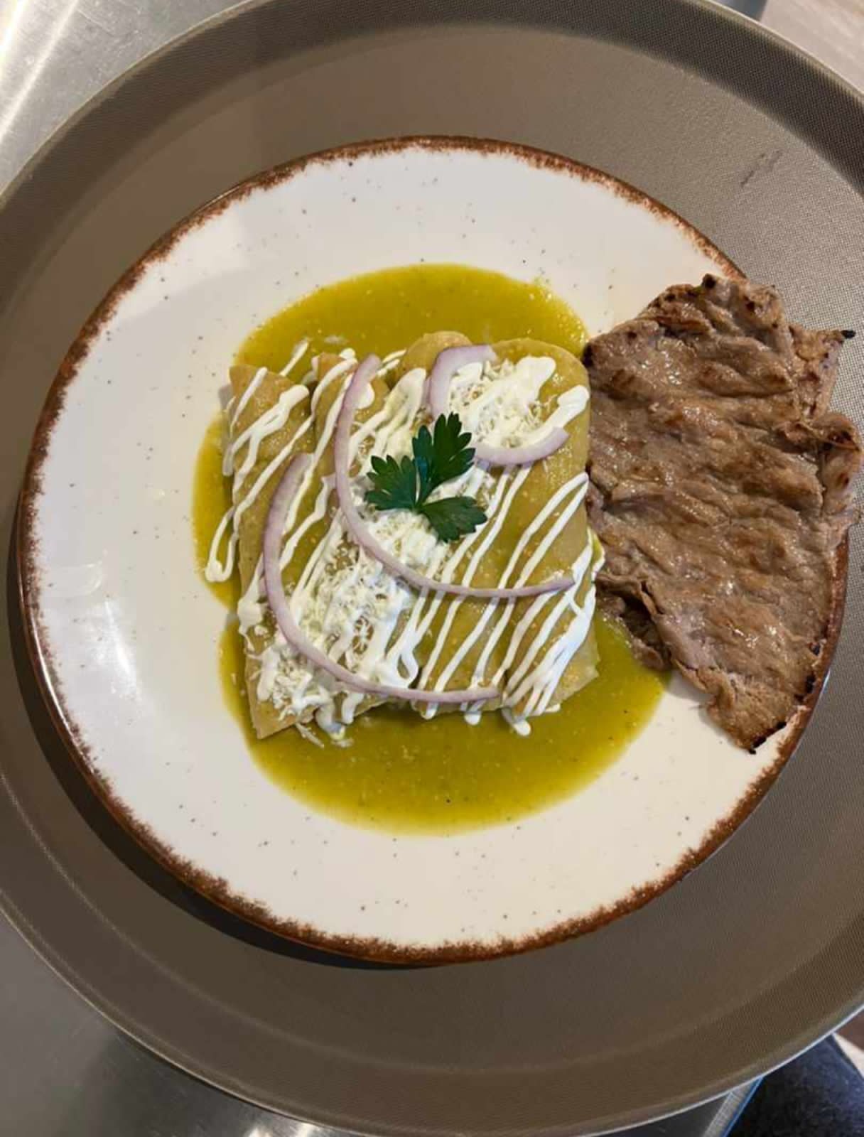 A plate with a dish that includes a piece of meat, a dollop of sauce, and a garnish.