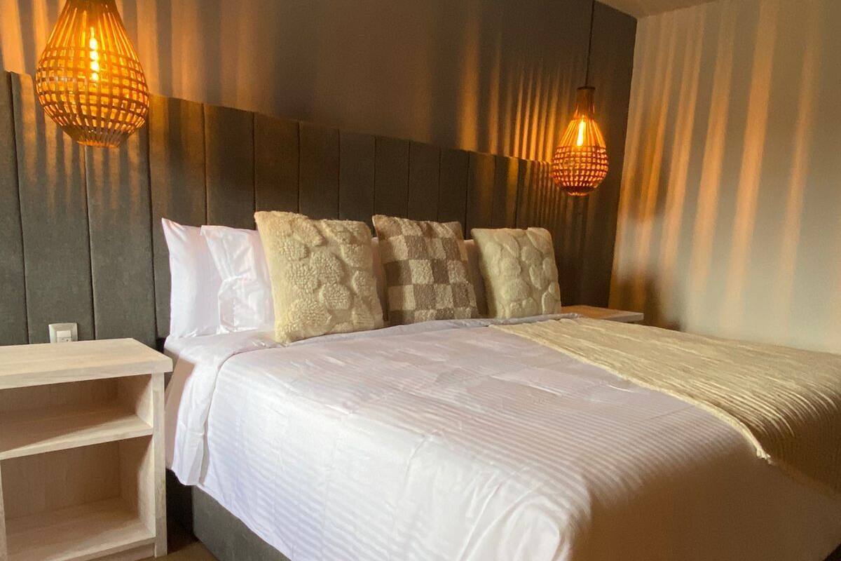 A modern bedroom with a large bed, two bedside tables, and two hanging lamps.