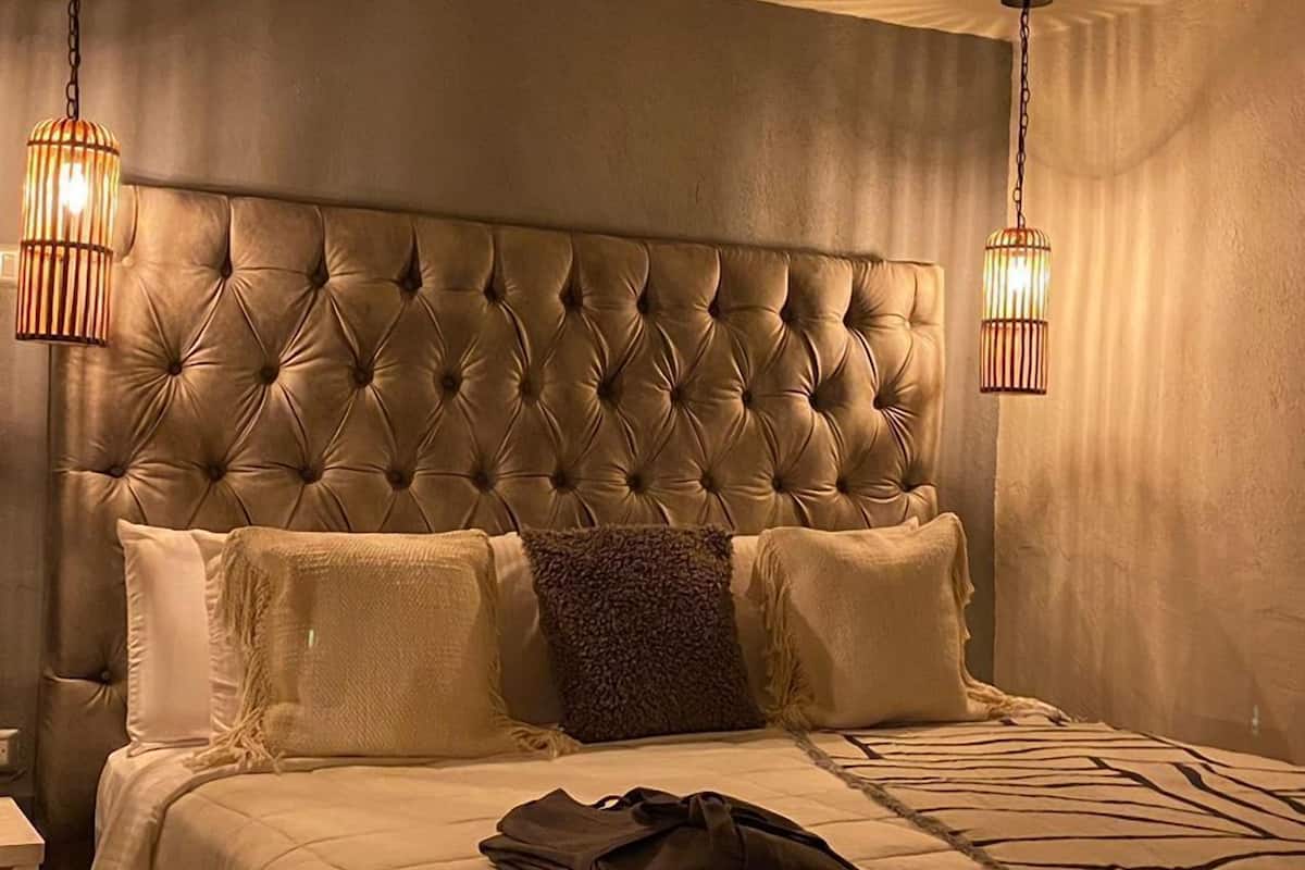 A bedroom with a tufted headboard, two bedside lamps, and a neatly made bed with a folded blanket.