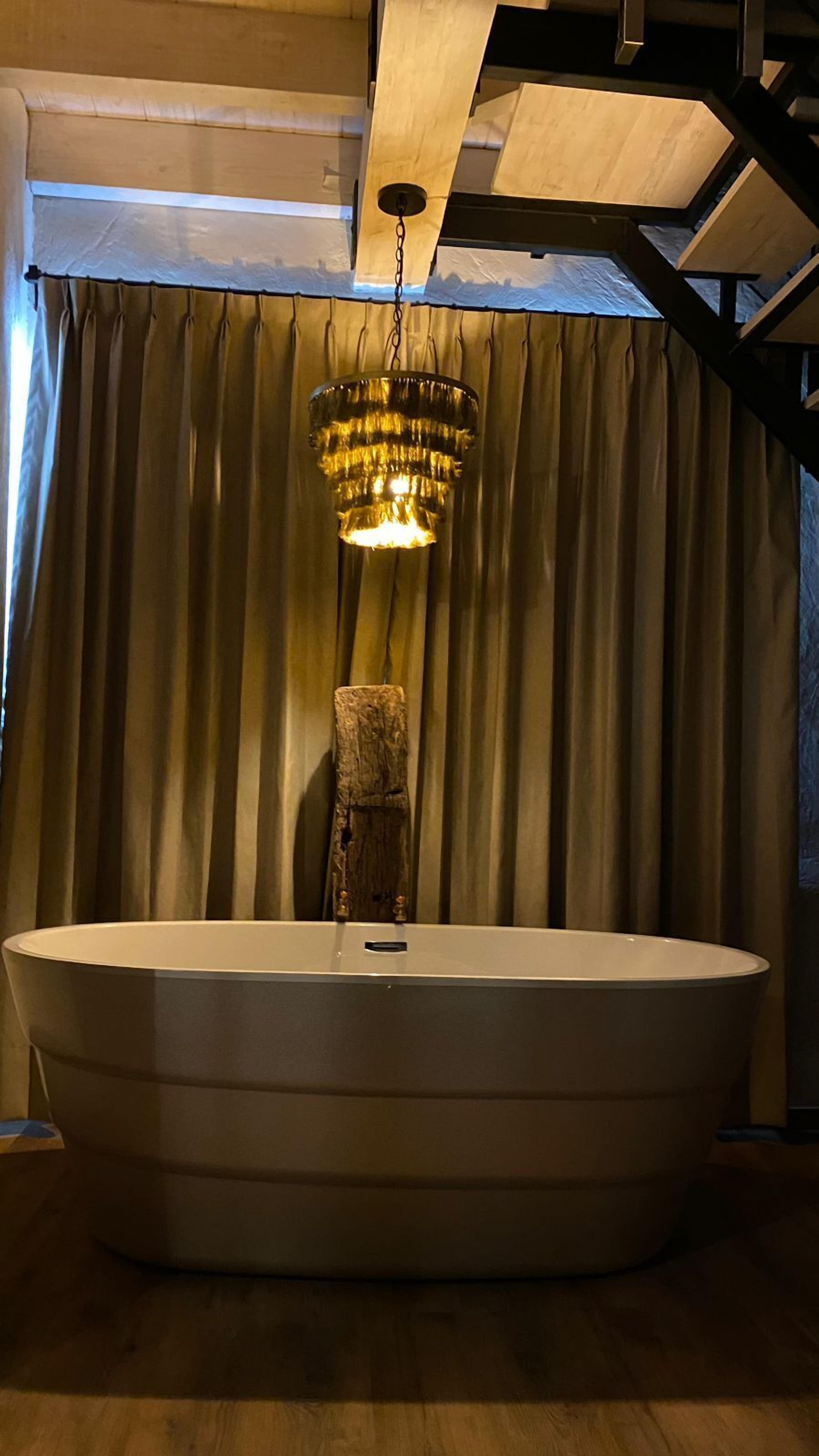 A large bathtub in a room with wooden beams and a curtain backdrop.