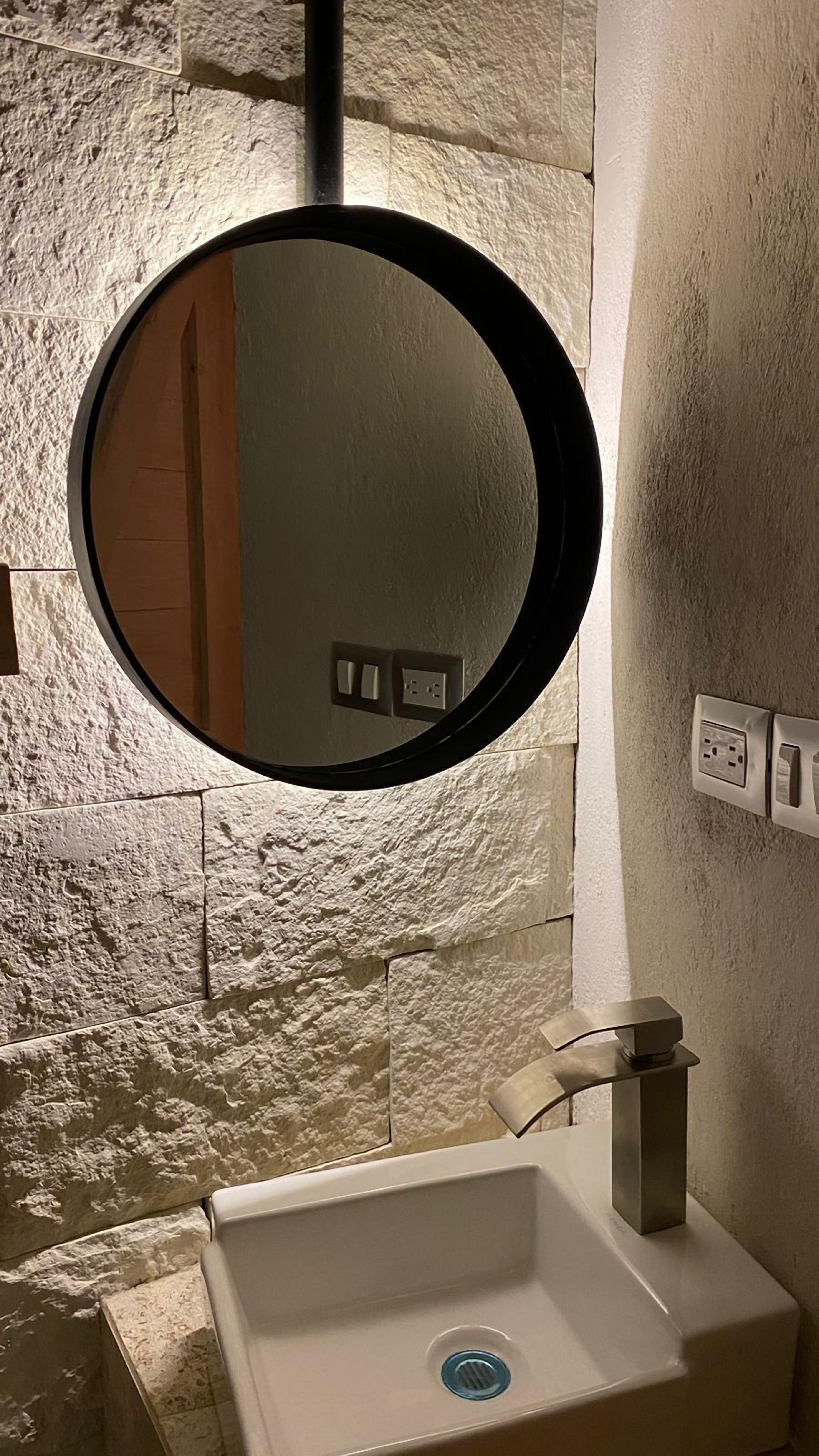 Ein Badezimmer mit rundem Spiegel, Waschbecken und einer wandmontierten Lampe.