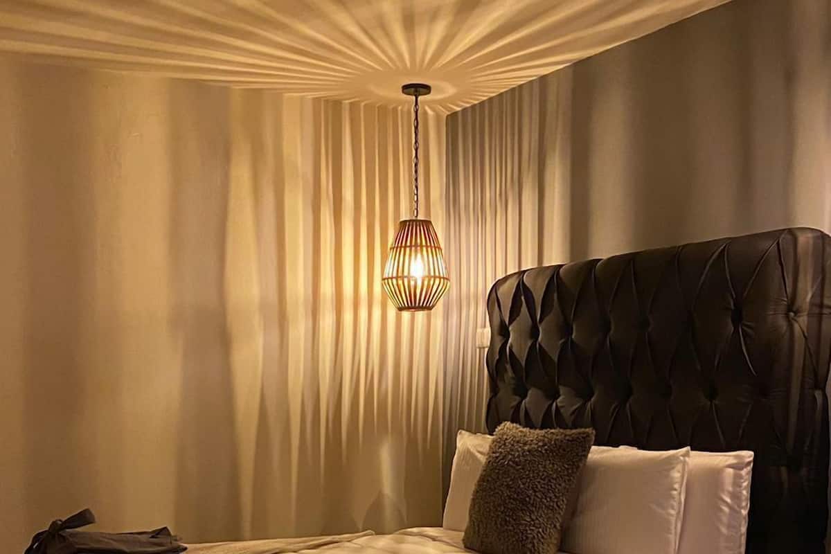 A bedroom with a tufted headboard, a large bed with a quilted cover, a hanging light fixture, and a wooden nightstand.