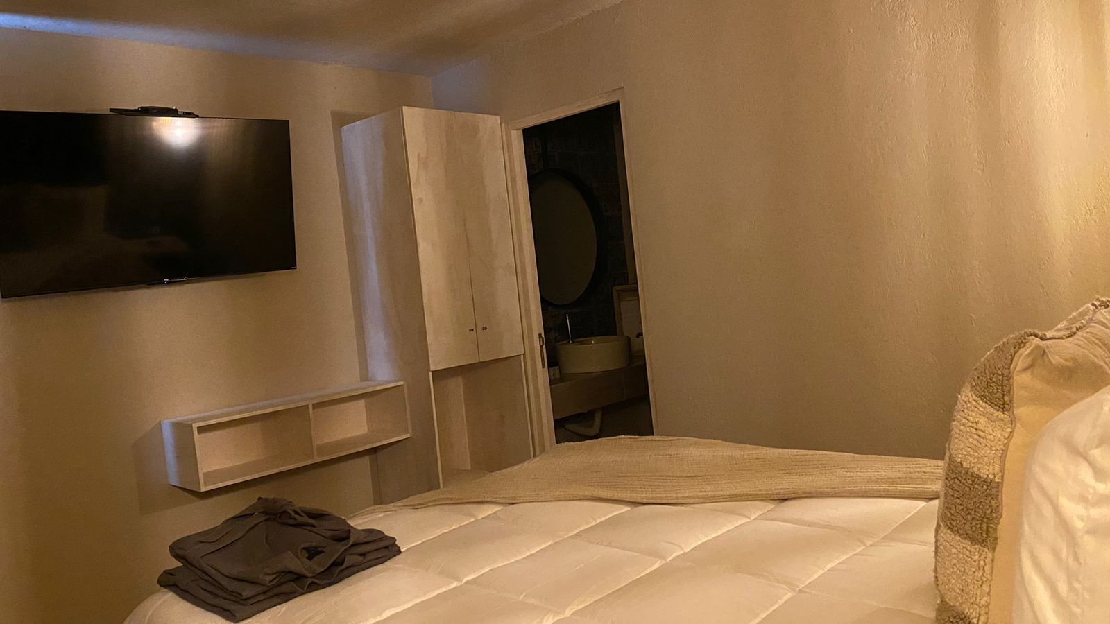 A bedroom with a bed, a TV mounted on the wall, a wardrobe, and a mirror.