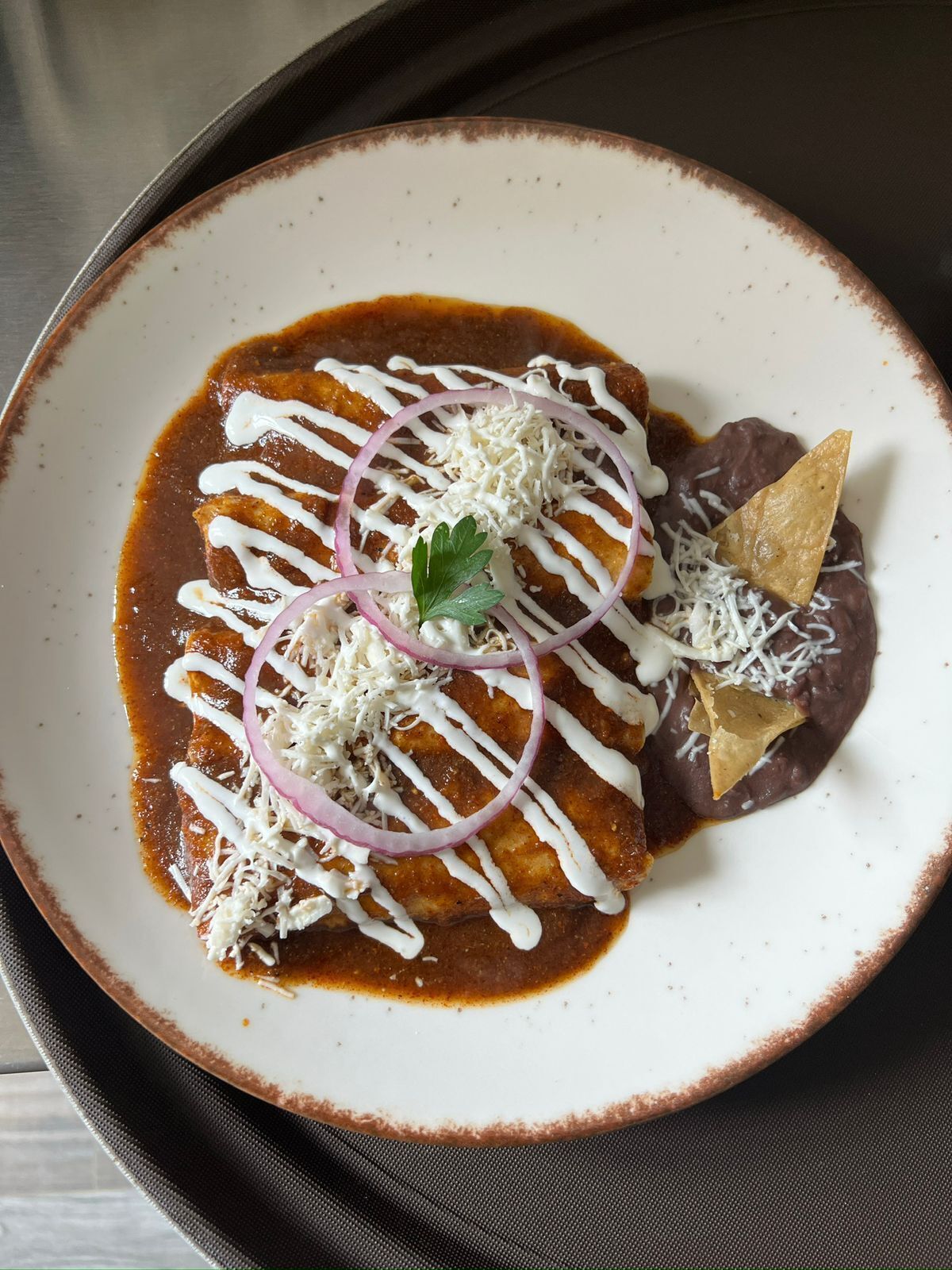 Ein Teller Enchiladas mit weißer Sauce, geriebenem Käse und einem Tortilla-Chip.