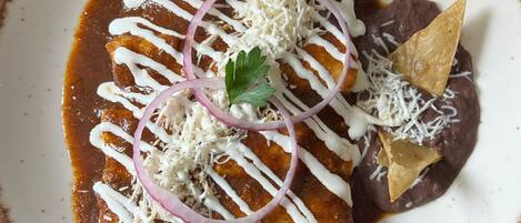Ein Teller Enchiladas mit weißer Sauce, geriebenem Käse und einem Tortilla-Chip.