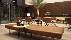 Een moderne loungeruimte met lederen zitplaatsen, een centrale boom en een receptiebalie.
