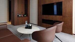 A modern room with a large flat-screen TV mounted on the wall, a round coffee table, and brown leather chairs. - ALMA Hotel Riyadh (Riyadh)