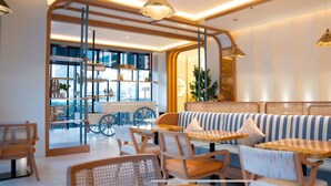 Een modern interieur met een zithoek met gestreepte banken en houten tafels, een glazen scheiding met een fiets, en uitzicht op de stadsgezicht.