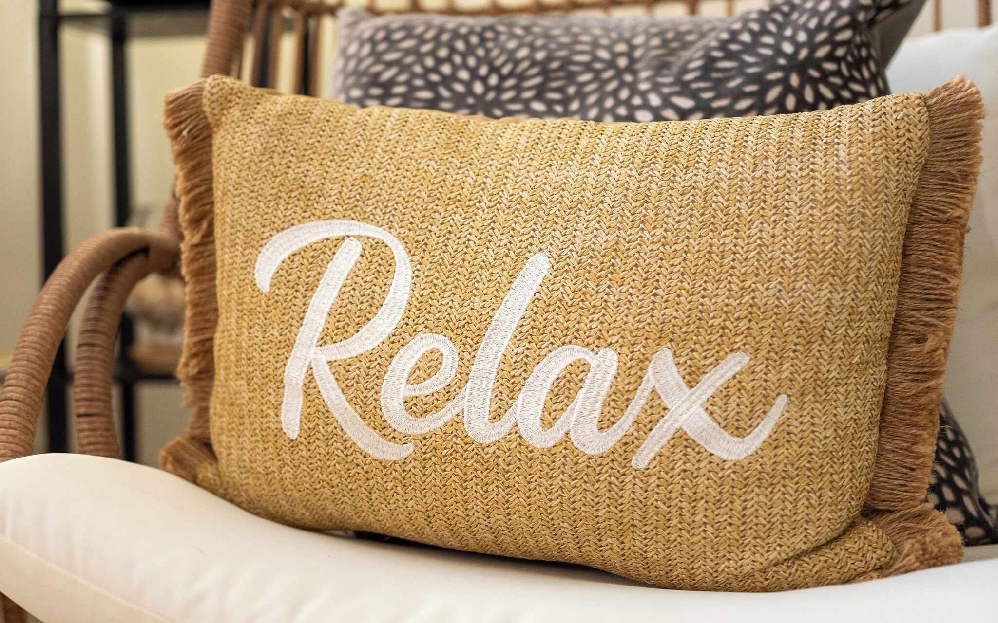 A woven pillow with the word "Relax" embroidered on it, placed on a white chair.