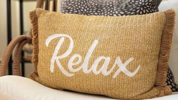 A woven pillow with the word "Relax" embroidered on it, placed on a white chair.