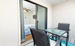 A balcony with a glass door leading to a bedroom, a table with chairs, and a ceiling fan. - Steps to Beach | Private Balconies | Relax Here (Jacksonville Beach)