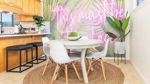 A modern kitchen with a round dining table, white chairs, and a neon sign on the wall. - Steps to Beach | Private Balconies | Relax Here (Jacksonville Beach)